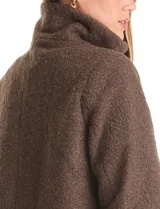 Tapado de tejido bouclé color marrón, con silueta evasé y largo a la cadera. Presenta cuello alto envolvente, cierre frontal oculto con botones a presión y bolsillos frontales de gran tamaño. Sus mangas son 3/4 con corte amplio y puños de tejido rib al tono que se extienden para cubrir las muñecas.