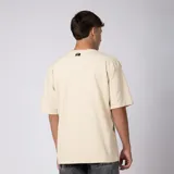Remera oversized de algodón grueso con textura micropanal, color beige, de cuello redondo y manga corta, con costura decorativa en "X" en el escote y diseño liso sin logos.