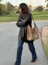 Cartera tipo hobo de cuero con estampado animal print de leopardo, con tiras y detalles en cuero rojo con flecos y parche rectangular con logo grabado en la parte frontal.