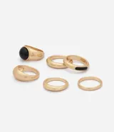 Kit de seis anillos dorados de metal con diseño bold y orgánico, que incluye piezas de diferentes grosores y detalles con incrustaciones de resina negra.