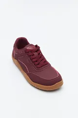 Zapatilla de estilo barefoot color marrón, confeccionada con una combinación de gamuza y materiales sintéticos. Presenta un diseño de perfil bajo con suela de goma flexible en color caramelo que incluye el logo de la marca grabado en el lateral.