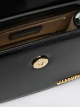 Bolso de mano estructurado de cuero color negro, con asa corta rígida, cierre con solapa y broche metálico dorado. Incluye correa fina desmontable y ajustable para usar como bandolera. Logotipo de la marca en letras doradas en la parte inferior frontal.