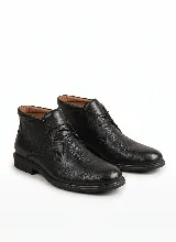 Bota corta tipo botineta de cuero negro con textura granulada, cierre mediante cordones y suela plana de goma.