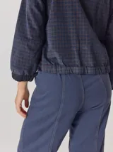 Pantalón de corte relajado color marrón oscuro, con costuras en hilo rojo a contraste y bordado decorativo en el bolsillo delantero.