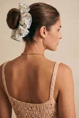 Scrunchie de tela blanca con estampado de pequeñas flores azules y borde con volados ribeteados en celeste.