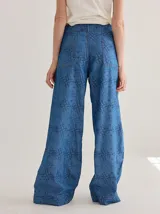 Pantalón de jean de corte ancho y tiro medio, con estampado de monograma en color azul oscuro sobre base de denim azul claro. Presenta cierre frontal con botón y costuras a la vista.
