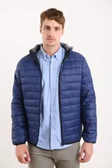 Campera capitoneada color azul marino, con capucha de algodón gris desmontable y cierre frontal. Tiene dos bolsillos exteriores con cierre.