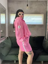 Buzo oversize de plush color rosa chicle, con cuello alto, cierre frontal parcial, capucha y bolsillo tipo canguro. Presenta puños elásticos y cordón ajustable en el ruedo.