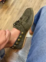 Náuticos de gamuza color suela con flecos en la parte delantera y detalle de tachas metálicas circulares en el lateral. Diseño artesanal con cordones frontales y suela plana.