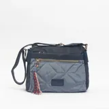 Bandolera de diseño bicolor en tonos azul y gris, con cuerpo acolchado en forma de rombos. Incluye cierre frontal con cremallera dorada, detalle de borla decorativa con cordones trenzados y correa ajustable para el hombro.