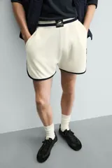 Short deportivo de tejido de punto con estructura abierta, color blanco con vivos a contraste en azul marino. Presenta cintura elástica, bolsillos frontales, aberturas laterales en el bajo y etiquetas conmemorativas de la Copa Mundial de la FIFA Francia 98.