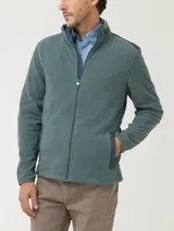 Campera polar RKF modelo Volterra color verde grisáceo, con cierre frontal completo, cuello alto y mangas largas. Presenta aplicaciones de tela canvas de algodón en los hombros, dos bolsillos frontales con cierre y bolsillos internos. Confeccionada en poliéster reciclado.