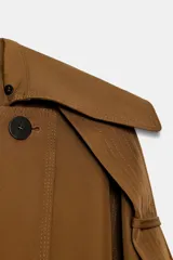 Trench largo color marrón, de corte amplio, con cuello solapa desmontable de pelo sintético marrón. Presenta cierre cruzado con botones oscuros y cinturón de tela anudado a la cintura.