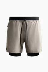 Short deportivo de doble capa color gris claro, con cintura elástica negra, cordón de ajuste y calza interna incorporada.