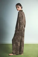 Pijama de dos piezas con estampado animal print de leopardo. Incluye una camisa de manga larga con cuello camisero y cierre frontal de botones, y un pantalón de corte recto y holgado con cintura elástica.