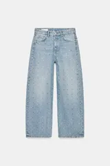 Pantalón de jean estilo baggy con tiro medio, corte holgado y diseño de cinco bolsillos. Presenta un acabado en lavado claro con aplicación de brillos distribuidos por toda la prenda.