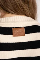 Sweater de punto a rayas horizontales negras y crudas, con cuello redondo y mangas largas. Tiene ribete marrón en puños y ruedo.