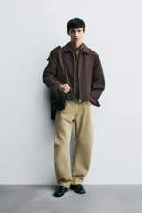 Cazadora cropped fit color marrón oscuro, confeccionada en tejido de algodón. Presenta cuello solapa, manga larga con puño abotonado, bolsillos de vivo en la cadera y un bolsillo interior. El bajo tiene elástico en la espalda y el cierre es frontal con cremallera.