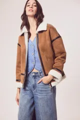 Campera marrón de gamuza sintética con cuello, puños y ruedo de piel sintética blanca. Presenta cierre frontal con cremallera, bolsillos laterales y detalles en cuero sintético negro.