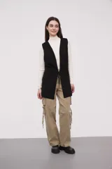 Chaleco largo sin mangas de tejido de punto color negro, con capucha y lazo ajustable en la cintura. Presenta bolsillos frontales y diseño abierto.