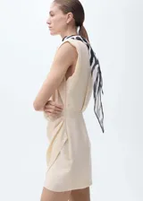 Vestido corto color crema, con escote en V cruzado, sin mangas y falda cruzada con drapeado lateral.