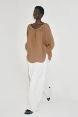 Blusa de lino color amarillo pastel, con escote recto ajustable mediante lazadas, hombros descubiertos y mangas largas abullonadas con puños elásticos.