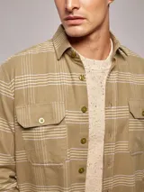 Sobrecamisa de manga larga en color verde oliva con estampado de cuadros finos. Presenta cuello clásico, cierre frontal con botones y dos bolsillos frontales con solapa y botón.