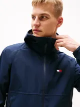 Campera cortavientos azul marino de corte amplio, con capucha fija, cuello alto, cierre de cremallera, dos bolsillos delanteros con cremallera y forro con diseño integral de la insignia de Tommy.