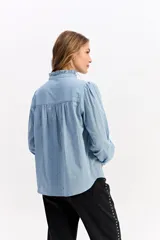 Blusa de algodón en color celeste, con textura sutil, cuello con volados y mangas largas con puños también decorados con volados. Presenta cierre frontal con botones.