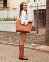 Bota de caña alta confeccionada en cuero color marrón tostado. Presenta un diseño con tres hebillas decorativas en la parte superior de la caña y una correa con hebilla y argolla metálica en el tobillo. Cuenta con suela plana y taco bajo de madera oscura.