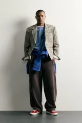 Blazer de corte boxy fit de Zara, confeccionado en tejido con algodón con estampado a cuadros en tonos beige, negro y blanco. Cuenta con cuello de solapas de muesca, manga larga con botones en los puños, bolsillos de vivo en el pecho y de plastrón en la cadera, y cierre frontal con un botón.