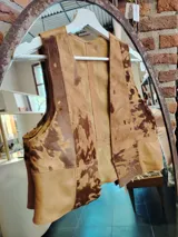 Chaleco de cuero con diseño de parches que combinan cuero liso y cuero con pelo, presentando un patrón de manchas tipo animal print vacuno en tonos marrones y beige.