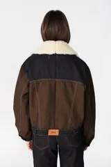 Chaqueta de denim color marrón con costuras en contraste, cuello de lana desmontable en color crema, cierre frontal con botones metálicos y bolsillos laterales.