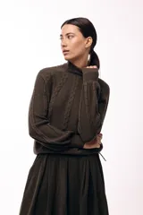 Polera de tejido de punto color marrón, con cuello alto y diseño de trenzas verticales. Presenta mangas largas con puños ajustados y un detalle de panel lateral asimétrico que se anuda en la cintura.