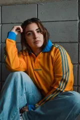 Camiseta de manga larga Adidas Originals, de corte holgado y color amarillo con rayas verticales sutiles en tono más oscuro y detalles en azul en cuello polo, puños y las clásicas franjas en las mangas. Cuenta con el logo bordado en el pecho.