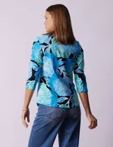 Remera de algodón estampada con flores en tonos celeste, azul y verde, sobre fondo negro. Tiene mangas 3/4 y escote cuadrado.