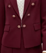 Blazer de sastrería color bordó, de corte slim, con solapas clásicas, cierre frontal cruzado con botones dorados y bolsillos laterales con solapa.