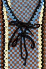 Vestido corto sin mangas confeccionado en tejido a crochet con diseño de damero en tonos celeste, marrón y blanco. Presenta escote en V con cordones negros para ajustar.