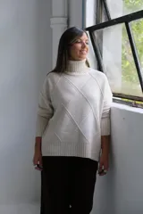 Polerón de cuello alto con diseño de rombos tejidos en relieve, mangas largas con puños acanalados y ruedo asimétrico con aberturas laterales.