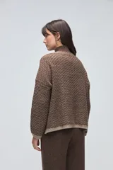 Cardigan de tejido de punto con textura, silueta boxy y cuello en V. Presenta cierre frontal con botones y detalles de terminación en contraste de color en los bordes.