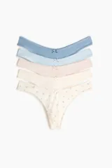 Pack de cinco bombachas tipo colaless de algodón, de tiro bajo con cintura en V, bordes con acabado picot y detalle de lazo pequeño en el centro. Incluye tres lisas en tonos azul, celeste y rosado, y dos con estampado floral pequeño sobre base clara.
