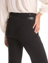 Pantalón de vestir negro con corte recto y tiro alto, confeccionado en tejido elastizado. Presenta una pretina trasera con detalle de ribete en cuero sintético y botones decorativos.