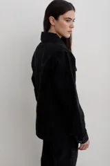Chaqueta de denim negro, de corte entallado en la cintura, con cuello clásico, cierre frontal de botones metálicos y bolsillos con solapa en el pecho.