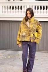 Campera de diseño artístico con estampado abstracto en tonos amarillos y marrones, cuello alto, cierre frontal con botones metálicos y bolsillos frontales con la palabra CAPER aplicada.