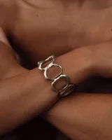 Brazalete rígido de diseño orgánico, compuesto por eslabones irregulares unidos entre sí, con acabado metálico brillante.