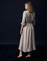 Vestido maxi color beige, con cuello mao y escote en V. Presenta mangas largas con presilla y botón para regular el largo, y un lazo ajustable en la cintura que marca la silueta.