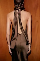 Vestido largo de satén color marrón, con cuello halter y espalda descubierta con cierre de cremallera y lazada.