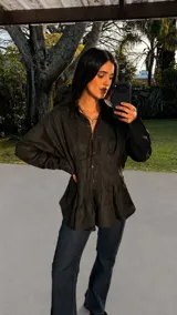 Camisa negra de silueta femenina con entalle en la cintura, realzado por alforzas gruesas, abertura frontal con botones y cuello clásico.