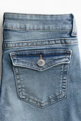 Jean de denim elástico color celeste claro, de tiro bajo y corte acampanado desde la rodilla. Cuenta con bolsillos abiertos delanteros, bolsillos traseros con solapa y botón, y cierre frontal con cremallera y botón metálico.