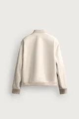 Campera bomber color verde militar de corte relaxed fit, confeccionada en tejido efecto ante, con cuello, puños y dobladillo en rib elástico, bolsillos frontales de vivo y cierre central con cremallera.